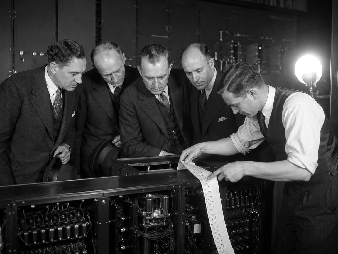 Engineers reading a strip of punched tape at a calculating machine